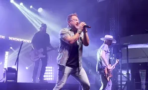 A band performs on a brightly lit stage with purple and white lights.