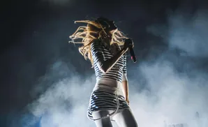Singer with blonde hair in a striped outfit performs on stage with smoke effects.
