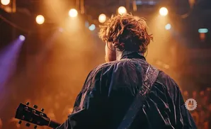 Guitarist playing on stage with warm lighting and audience in background.