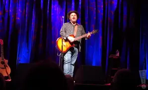 martin sexton playing the electric guitar and singing in front of dark blue curtain