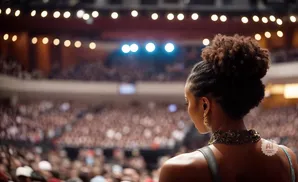 Woman with hair in a bun looks out at a large, blurred audience in an arena, with bright lights overhead.
