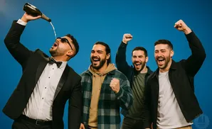 Four men celebrate with champagne and raised fists against a blue background.