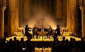 Four musicians play string instruments in a candlelit hall.