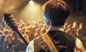 Musician playing guitar on stage with a blurred crowd in the background.