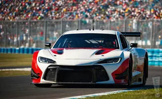 A white and red race car with a spoiler speeds around a track, with a blurred crowd in the background.