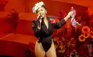 Singer Janelle Monáe performs in a black leotard and blazer, wearing a flower crown and holding a bouquet.
