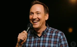 A man in a plaid shirt smiles and holds a microphone.