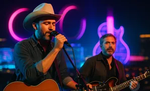 A country singer in a cowboy hat performs with a band on a stage with neon guitar and circle accents.