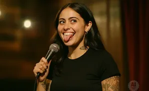 A woman with dark hair sticks her tongue out while holding a microphone.