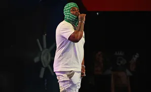 Rapper with a green balaclava and white outfit, holding a microphone.