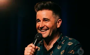 Comedian holding a microphone and laughing on stage.