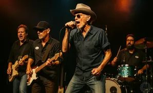 A rock band performs on stage, with a lead singer in a cowboy hat in the foreground.