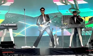 Two musicians perform on stage with guitars and keyboards.