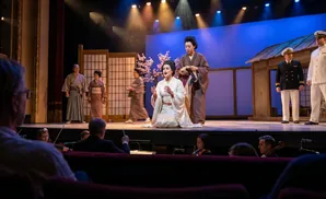 Stage performance with Japanese actors and sailors, with an orchestra in the foreground.