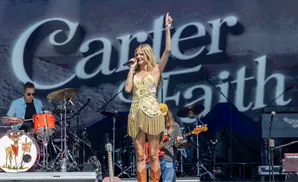Country singer Kelsea Ballerini performs live on stage wearing a sparkly dress and cowboy boots.