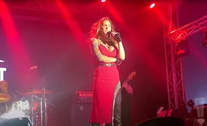 A woman in a red dress sings on stage with a band.