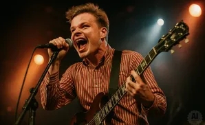 A man sings into a microphone while playing a guitar on stage.
