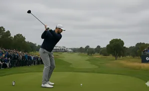 Golfer mid-swing on a tee box with a large crowd and golf course in the background.