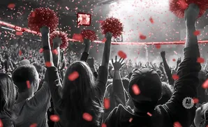Fans cheer and wave red pom-poms in a stadium with red confetti falling.