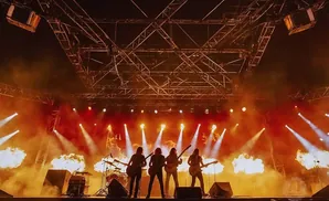 A rock band performs on a stage with dramatic lighting and pyrotechnics.