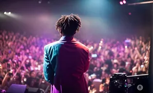 A performer with dreadlocks faces a crowd of fans holding up their phones at a concert.