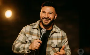 A man in a plaid jacket laughs while holding a microphone.