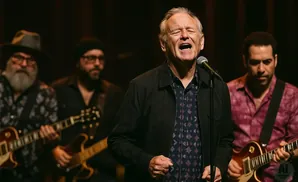 A band performs live, with the lead singer passionately singing into a microphone as guitarists play in the background.