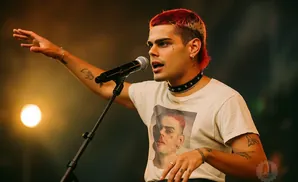A young man with red and blonde hair sings into a microphone, wearing a t-shirt with his own face printed on it.