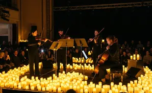 A string quartet performs on a stage lit by thousands of candles, with an audience in the background.