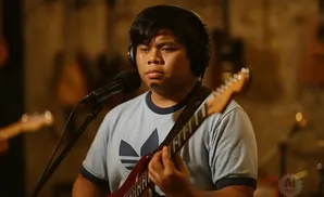 Man wearing headphones plays a red guitar and sings into a microphone.
