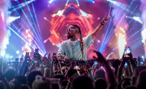 A DJ performs at a concert, with a crowd holding up phones to record.