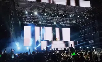 A DJ performs on stage at a concert with a large crowd in the foreground.