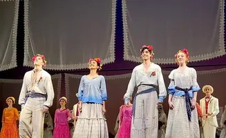 Dancers in floral headbands on stage, dressed in peasant-style clothing.