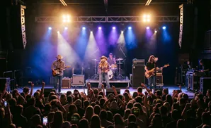 A country band performs on stage at a concert, with a large crowd in the foreground.