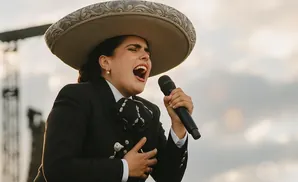 A mariachi singer in a sombrero and suit, singing into a microphone with her eyes closed.