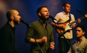 A band performs on stage with a lead singer in the foreground, accompanied by a guitarist and two other musicians.