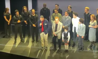 A diverse group of actors stand on a stage.
