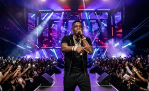 A rapper performs on stage with bright lights and a cheering crowd.