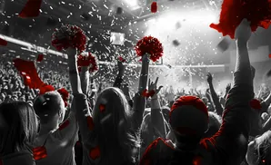 Crowd celebrating at an event with red confetti and pom-poms in the air.