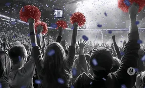 Fans cheer with red pom-poms at a concert, with confetti falling around them.