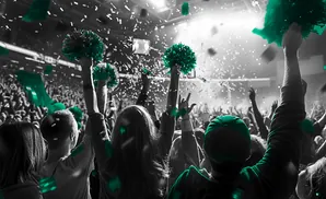 A crowd cheers and waves green pom-poms and flags with confetti falling.