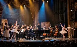 A ballet dancer performs with an orchestra and pianist on a stage.
