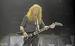 Dave Mustaine of Megadeth plays a black V-shaped guitar on stage with Marshall amps behind him.