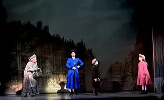 A stage production with actors dressed in Victorian-era clothing against a dark, painted cityscape backdrop.