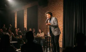 A comedian performs for a laughing audience in a dimly lit brick club.