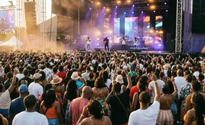 A large crowd of people are enjoying an outdoor concert with a stage and performers visible.