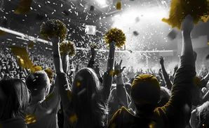 Crowd with raised hands and gold pom-poms throwing confetti during a celebration.