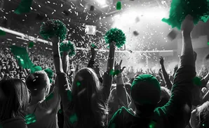 Crowd at a concert or event, celebrating with green pom-poms and confetti.