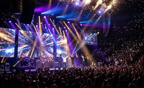 A band performs on stage under pink lighting, with guitars, drums, and keyboards visible.