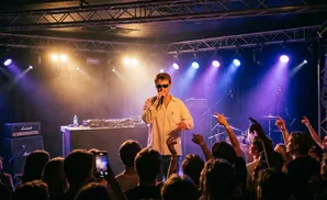DJ with laptop and equipment in front of a wall of pink and blue LED lights.